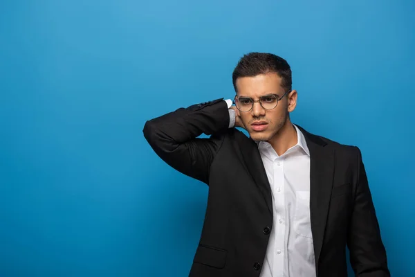 Pensive businessman with hand on back of head on blue background — Stock Photo