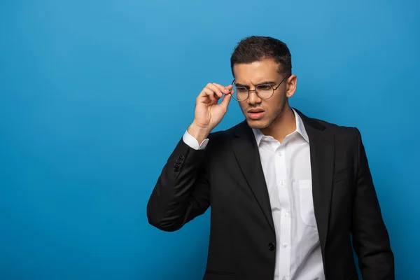 Задумчивый бизнесмен регулирует очки на синем фоне — стоковое фото