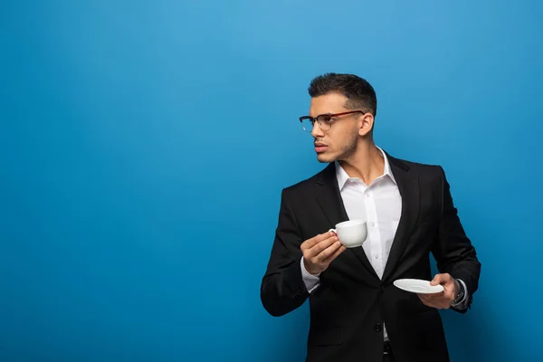 Handsome businessman with coffee cup looking away on blue background — Stock Photo