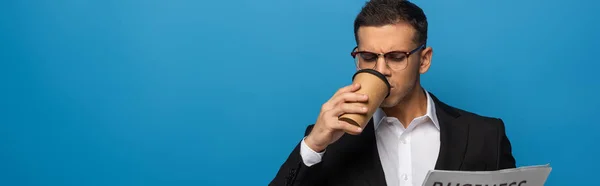 Panoramic shot of businessman drinking coffee and reading newspaper isolated on blue — Stock Photo