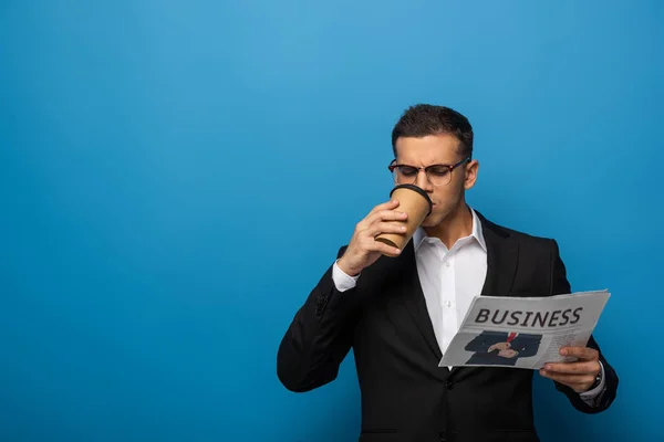 Bello uomo d'affari con caffè per andare a leggere il giornale su sfondo blu — Foto stock