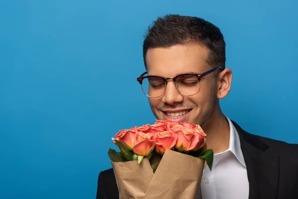 Hombre de negocios sonriente con los ojos cerrados sosteniendo ramo aislado en azul - foto de stock