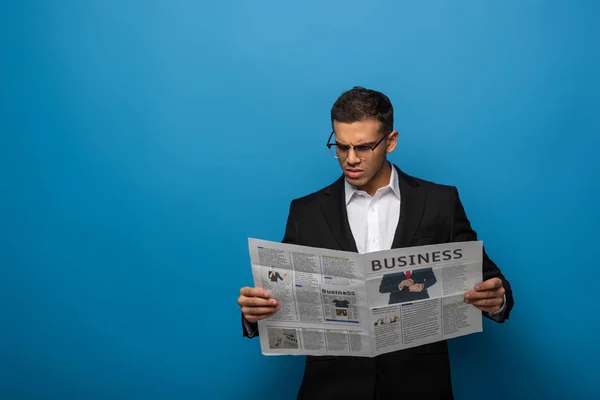 Nachdenklicher Geschäftsmann liest Zeitung auf blauem Hintergrund — Stockfoto