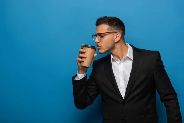 Seitenansicht eines jungen Geschäftsmannes mit Kaffee zum Gehen auf blauem Hintergrund — Stockfoto