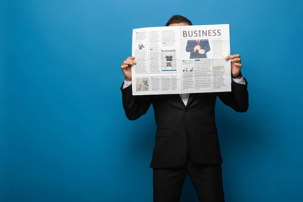Бизнесмен покрывает лицо газетой на синем фоне — стоковое фото
