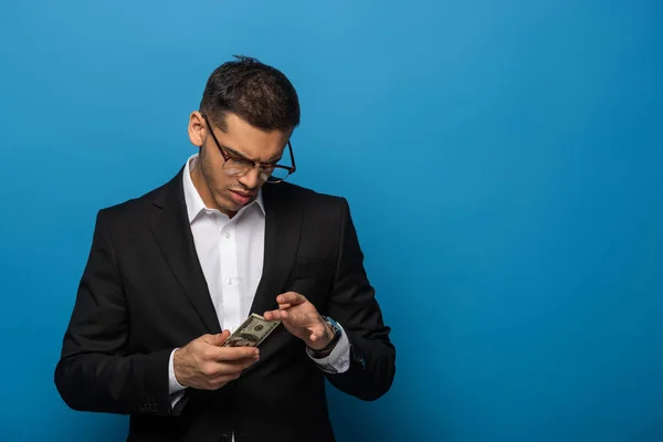 Schöner Geschäftsmann, der Dollarnoten auf blauem Hintergrund zählt — Stockfoto