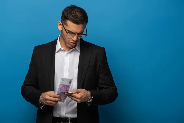 Jovem empresário contando notas de euro em fundo azul — Fotografia de Stock