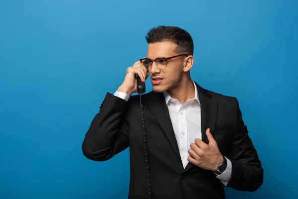 Handsome businessman talking on telephone on blue background — Stock Photo