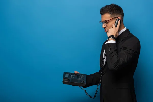 Vista lateral del hombre de negocios hablando por teléfono retro sobre fondo azul - foto de stock