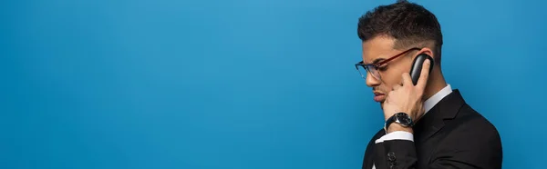 Vista lateral del hombre de negocios hablando por teléfono aislado en azul, plano panorámico - foto de stock