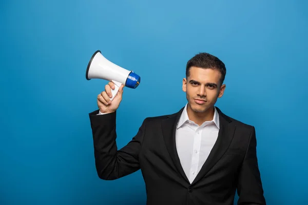 Schöner Geschäftsmann schaut in die Kamera, während er Lautsprecher auf blauem Hintergrund hält — Stockfoto