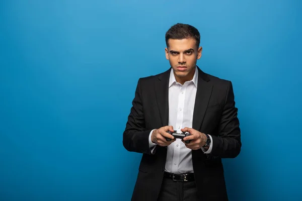 KYIV, UKRAINE - NOVEMBER 12, 2019: Handsome businessman with joystick looking at camera on blue background — Stock Photo