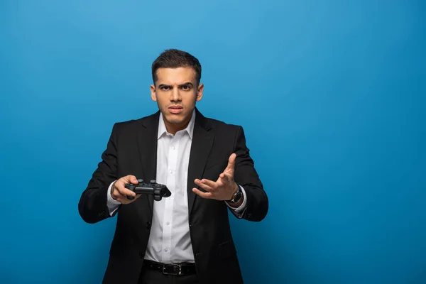 KYIV, UKRAINE - NOVEMBER 12, 2019: Businessman with joystick looking at camera and gesturing on blue background — Stock Photo