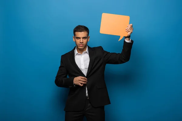 Handsome businessman holding speech bubble on blue background — Stock Photo