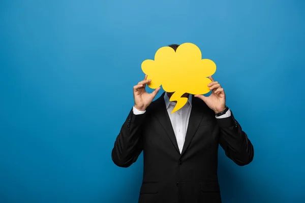 Hombre de negocios cubriendo la cara con burbuja del habla sobre fondo azul - foto de stock