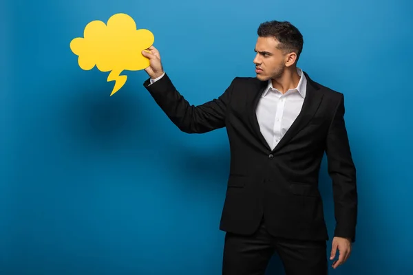 Vista lateral del hombre de negocios enojado mirando la burbuja del habla sobre fondo azul - foto de stock