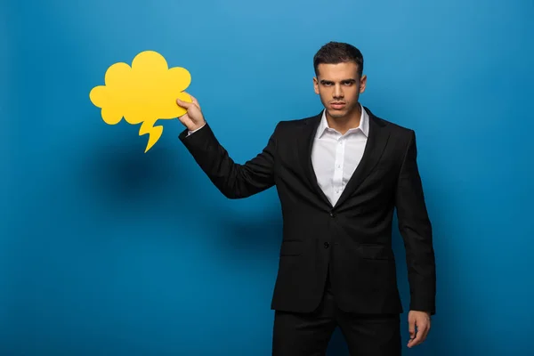 Beau homme d'affaires tenant bulle de discours et regardant la caméra sur fond bleu — Photo de stock