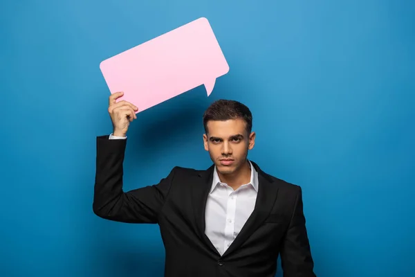 Young businessman with speech bubble looking at camera on blue background — Stock Photo