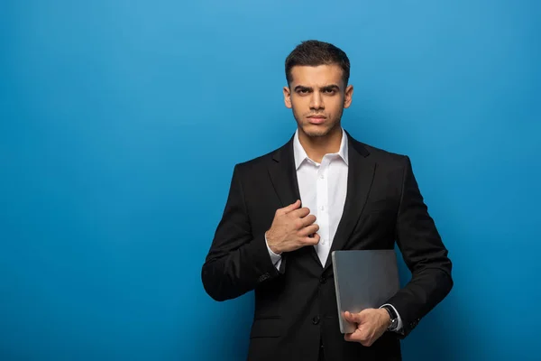 Beau homme d'affaires avec ordinateur portable regardant la caméra sur fond bleu — Photo de stock