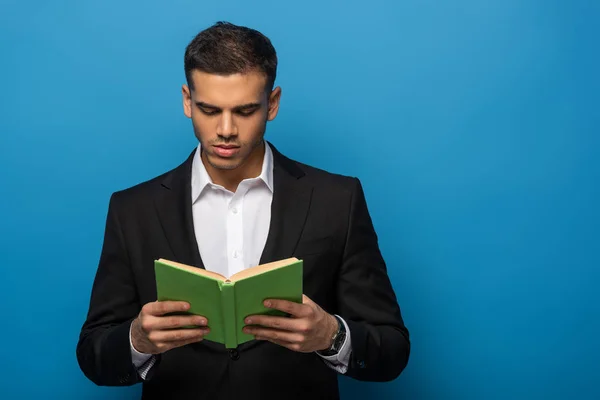 Young businessman reading book on blue background — Stock Photo