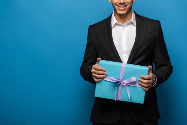 Vista recortada de hombre de negocios sonriente con regalo sobre fondo azul - foto de stock