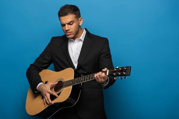 Jovem empresário tocando guitarra acústica em fundo azul — Fotografia de Stock