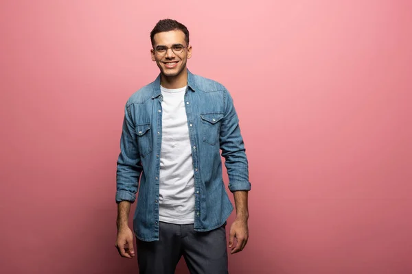 Handsome young man smiling at camera on pink background — Stock Photo