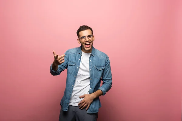 Fröhlicher junger Mann zeigt mit dem Finger auf Kamera auf rosa Hintergrund — Stockfoto