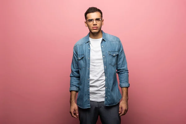 Handsome man in eyeglasses looking at camera on pink background — Stock Photo