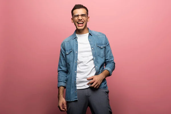 Schöner junger Mann mit Brille lacht auf rosa Hintergrund — Stockfoto