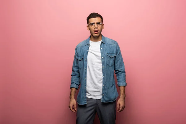 Shocked young man looking at camera on pink background — Stock Photo