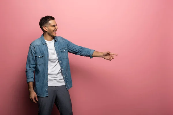 Вид сбоку смеющегося человека, указывающего пальцем на розовом фоне — стоковое фото