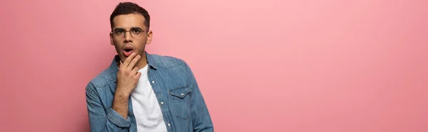 Panoramic shot of shocked man with hand by chin looking at camera on pink background — Stock Photo