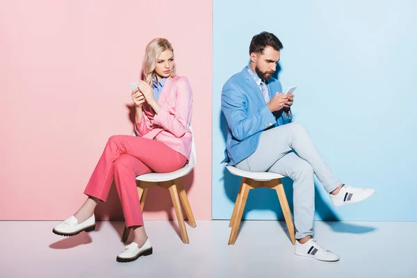 Suspicious woman looking at handsome man with smartphone on pink and blue background — Stock Photo