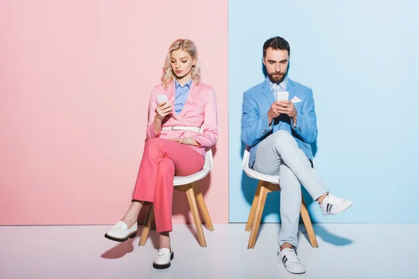 Atractiva mujer y hombre guapo utilizando teléfonos inteligentes sobre fondo rosa y azul - foto de stock