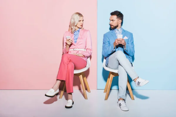 Mulher irritada e homem segurando smartphones no fundo rosa e azul — Fotografia de Stock