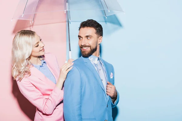 Donna sorridente con ombrello guardando bell'uomo su sfondo rosa e blu — Foto stock