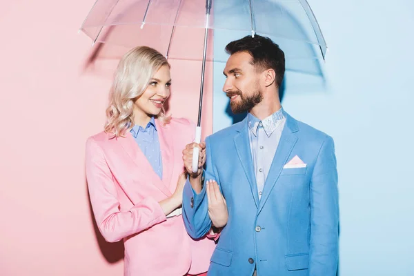Donna sorridente e bell'uomo con ombrello su sfondo rosa e blu — Foto stock