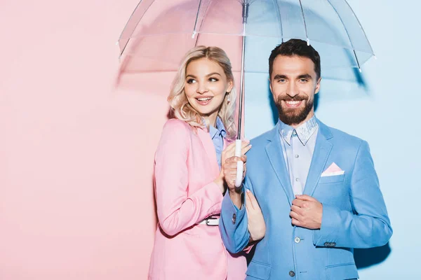 Donna sorridente e bell'uomo con ombrello su sfondo rosa e blu — Foto stock