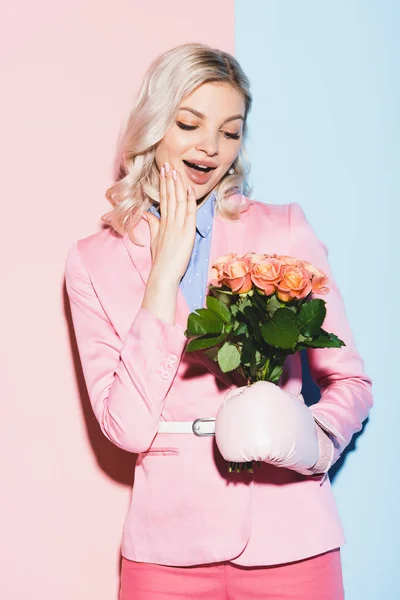 Shocked woman in boxing glove holding bouquet on pink and blue background — Stock Photo