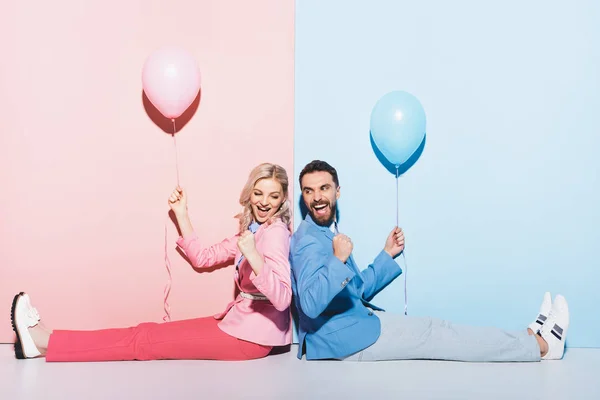 Zurück nach hinten Ansicht einer lächelnden Frau und eines gutaussehenden Mannes mit Luftballons, die eine Ja-Geste auf rosa und blauem Hintergrund zeigen — Stockfoto