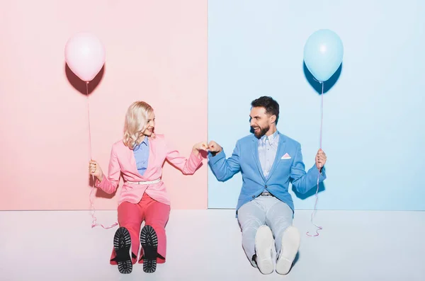 Smiling woman and handsome man with balloons showing fist to fist gesture on pink and blue background — Stock Photo