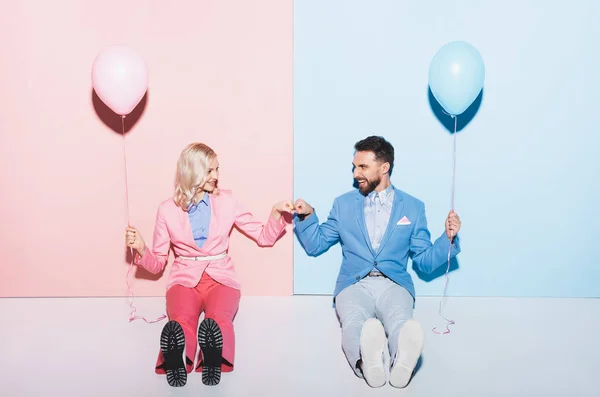 Mujer sonriente y hombre guapo con globos mostrando puño a puño gesto sobre fondo rosa y azul - foto de stock