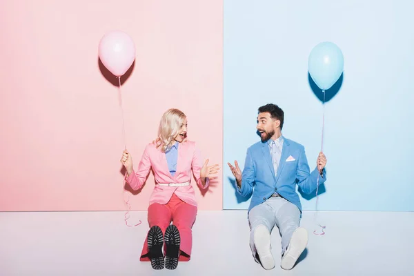 Шокована жінка і красивий чоловік тримає повітряні кулі на рожевому і синьому фоні — стокове фото