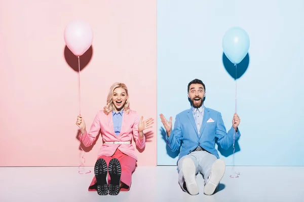 Shocked woman and handsome man holding balloons on pink and blue background — Stock Photo