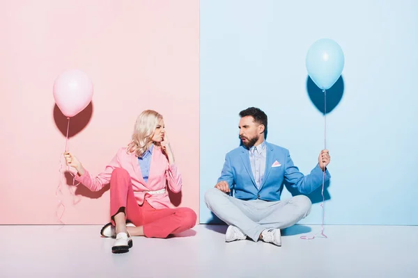 Donna attraente e bell'uomo con palloncini che fanno facce su sfondo rosa e blu — Foto stock