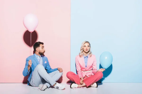 Attractive woman and shocked man holding balloons on pink and blue background — Stock Photo