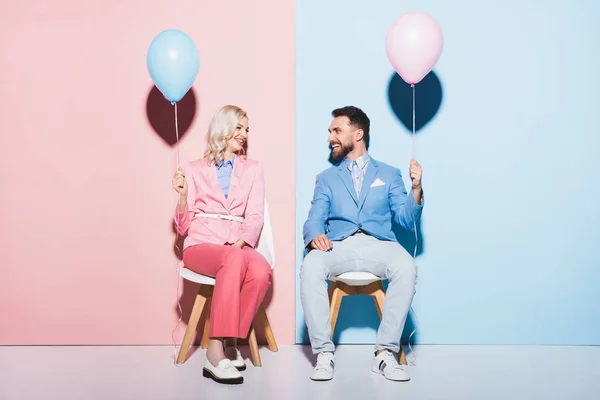 Smiling woman and handsome man holding balloons on pink and blue background — Stock Photo