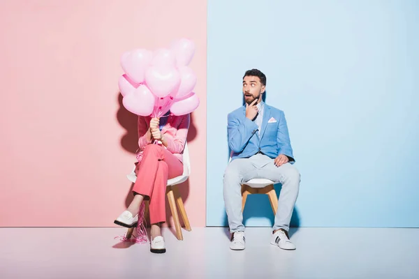 Woman holding balloons and shocked man on pink and blue background — Stock Photo