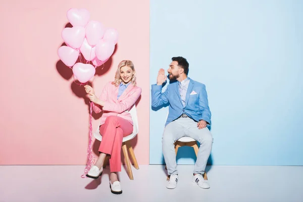 Mulher sorridente segurando balões e homem bonito no fundo rosa e azul — Fotografia de Stock